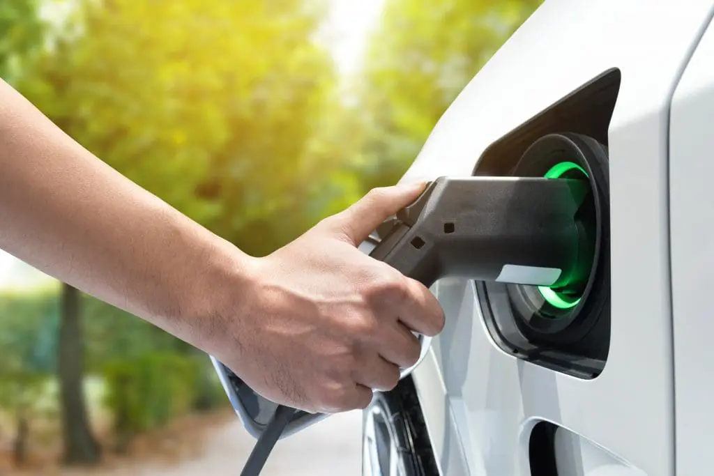 Electric vehicle charging station. Hand charging an electric car (EV) with the power cable supply plugged in.Flare light effect | Brandywine Valley Heating & Air Conditioning